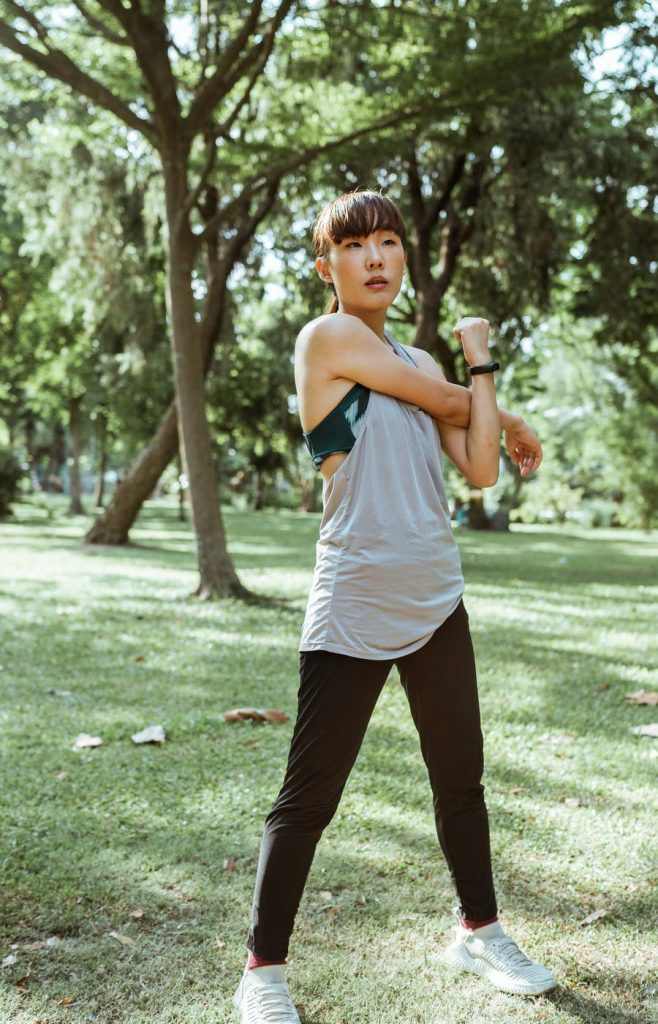 Woman wearing athletic clothes in a park stretching.