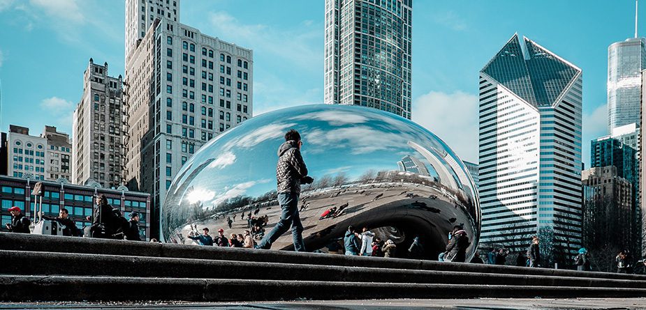 The famous Chicago Bean with a man walking in front and buildings in the background.
