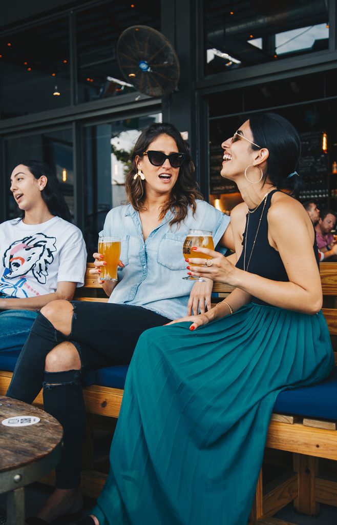 Women in an outdoor restaurant holding drinks and smiling.