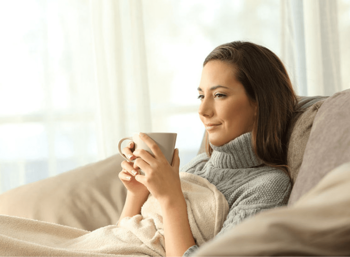 Woman drinking coffee under a blanket