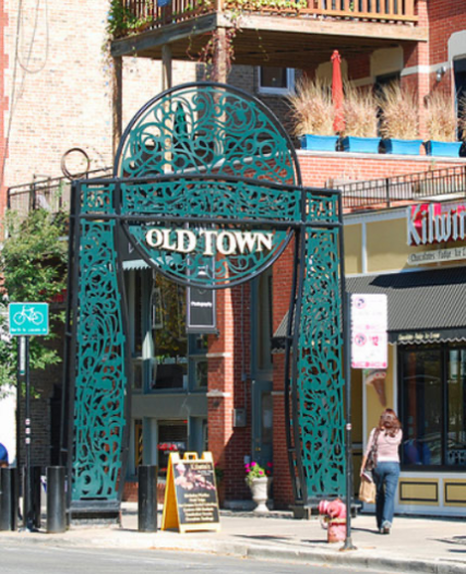 Old Town sign on metal archway in front of stores.